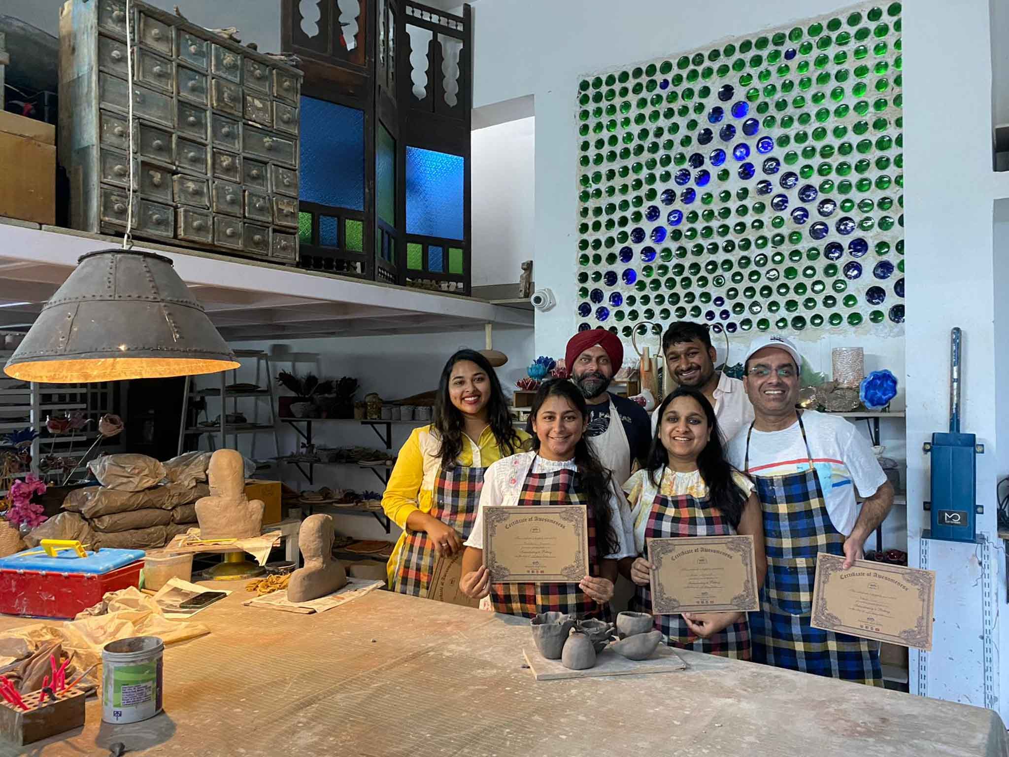 Group of pottery students holding certificates and standing in a pottery studio.